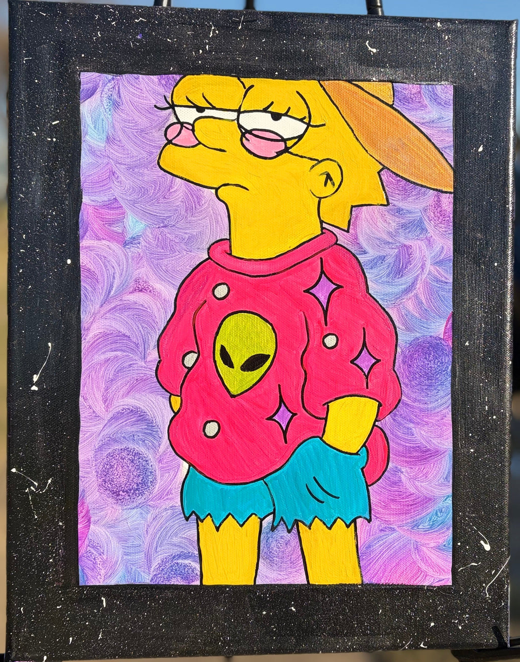 Colorful painting of a character with an alien design on a purple background, displayed on an easel outdoors.